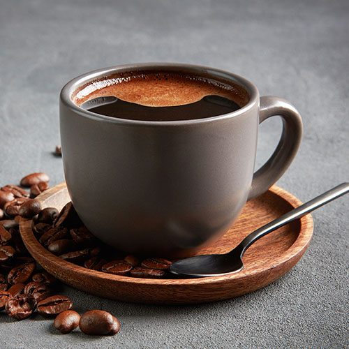 Freshly brewed black coffee in a ceramic cup surrounded by roasted coffee beans